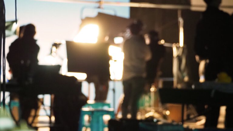 Warm production lights and crew out of focus behind the camera